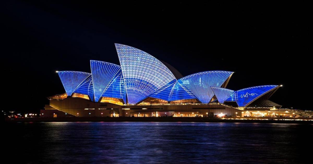Brightly lit Sydney Opera House illuminated with vibrant blue lights at night, iconic Australian landmark.