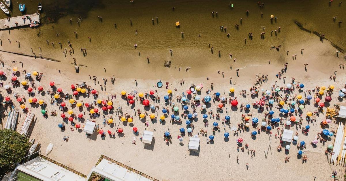 Colorful beach umbrellas and visitors at a sandy shoreline, sunny summer day, outdoor leisure, popular beach destination, QuestForDirections.