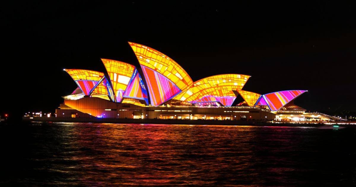 Colorfully lit Sydney Opera House illuminated at night with vibrant light display.