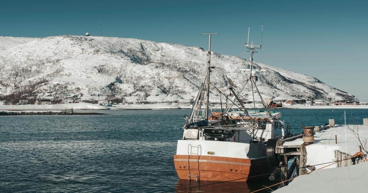 Snow-covered harbor with a boat, scenic mountain view, Norway, winter maritime landscape.