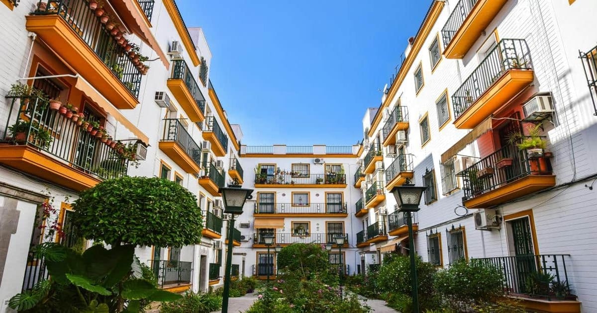 Colorful apartment buildings with balconies and lush greenery in a sunny urban courtyard.