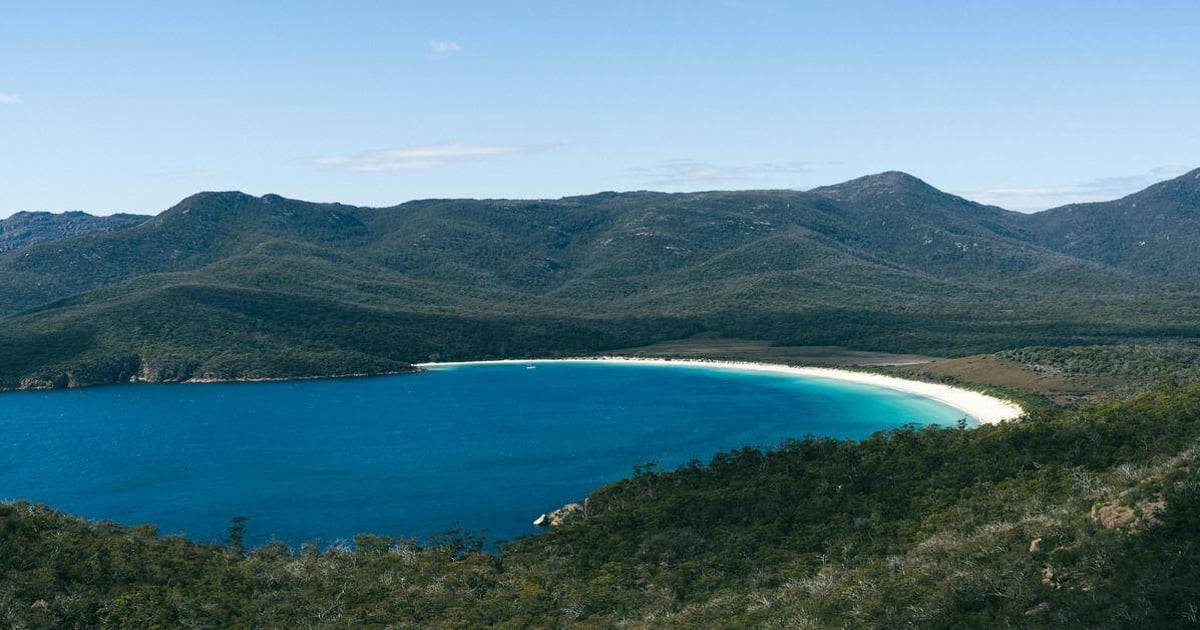 Pristine beach and turquoise waters around scenic wilderness bay with lush green mountains.