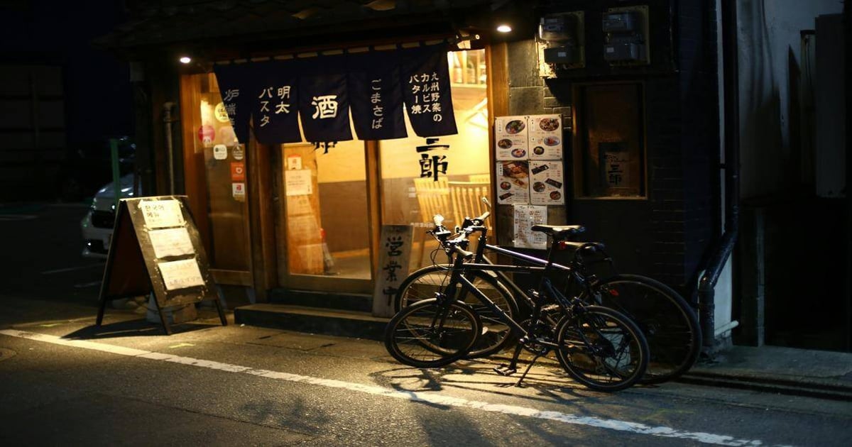 Cozy Japanese restaurant entrance with bicycles outside, illuminated at night, featuring traditional noren curtains.