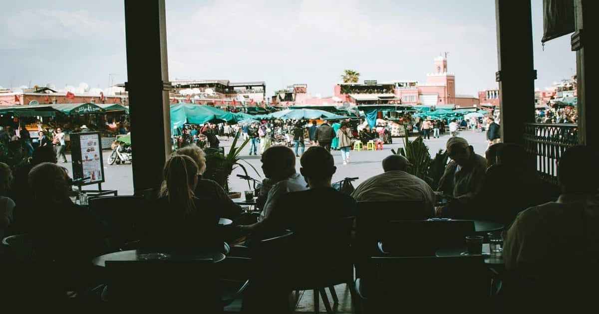 Busy market scene with outdoor vendors and shoppers, view from a café window in Morocco.